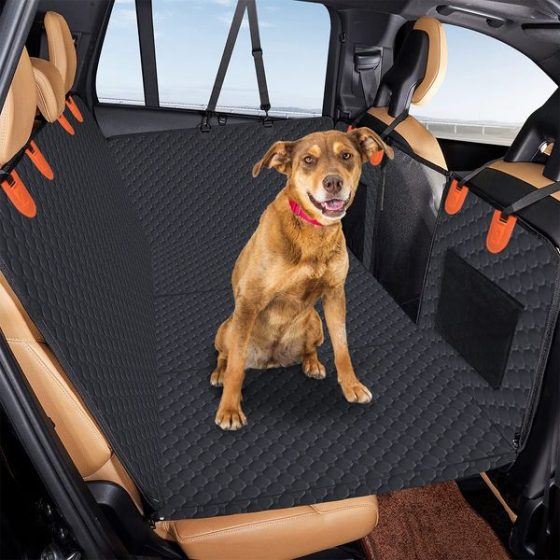 A brown dog sitting on a black quilted hammock cover installed across a vehicle rear seat.